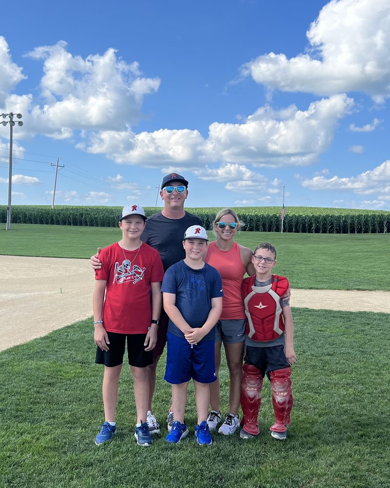 Jim with his family on a baseball field, a cornfield behind them